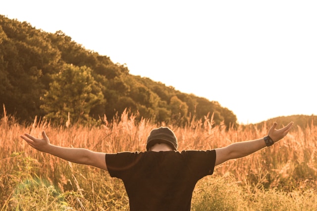 An image of a man standing in a field with arms spread wide worshipping Jesus